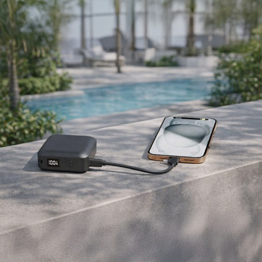DEKA power bank charging a phone on a stone ledge by a swimming pool