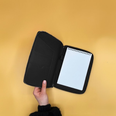 Open black INÉ Companion with inner pockets and spiral notepad, held over yellow background