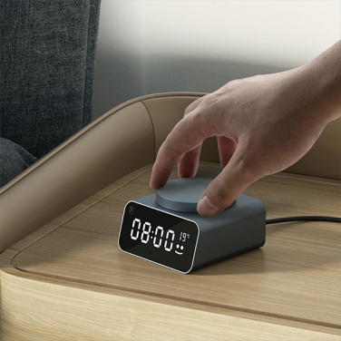 Hand pressing the button of an anthracite REDDI ALARM clock on a bedside table