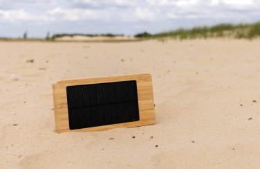 Pruun Sunwick 10 000 mAh bambusest päikeseakupank — horisontaalne kasutuspilt liival, logoga personaliseeritav, Logo.ee