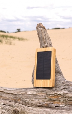 Ruskea Sunwick 10 000 mAh:n bambuinen aurinkovaravirtalähde — käyttökuva puupinnalla, personoitavissa logolla, Logo.ee