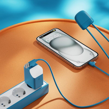 Zils ICE-G lādētājs pagarinātājā un ICE-C kabelis lādē iPhone uz oranža galda
