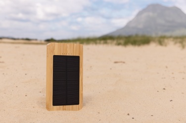 Brun Sunwick 10 000 mAh solcellspowerbank i bambu — stående miljöbild på sand, kan märkas med logotyp, Logo.ee