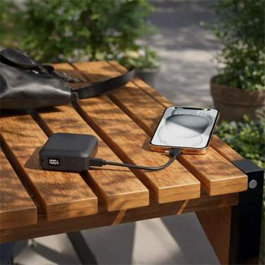 Svart DEKA powerbank laddar en smarttelefon på en parkbänk i trä